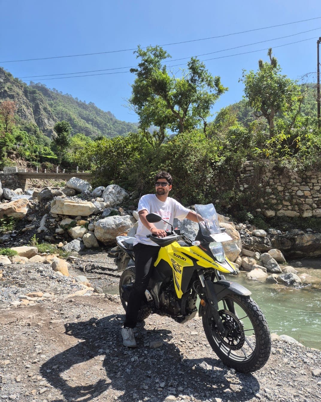 Tarush on a yellow adventure motorcycle beside a mountain river
